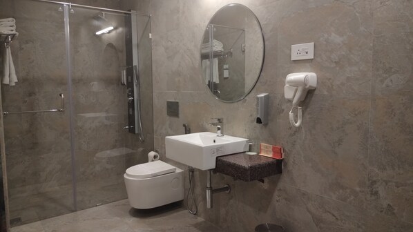 Un baño moderno con ducha de vidrio, inodoro blanco, lavamanos con espejo y secador de pelo montado en la pared.