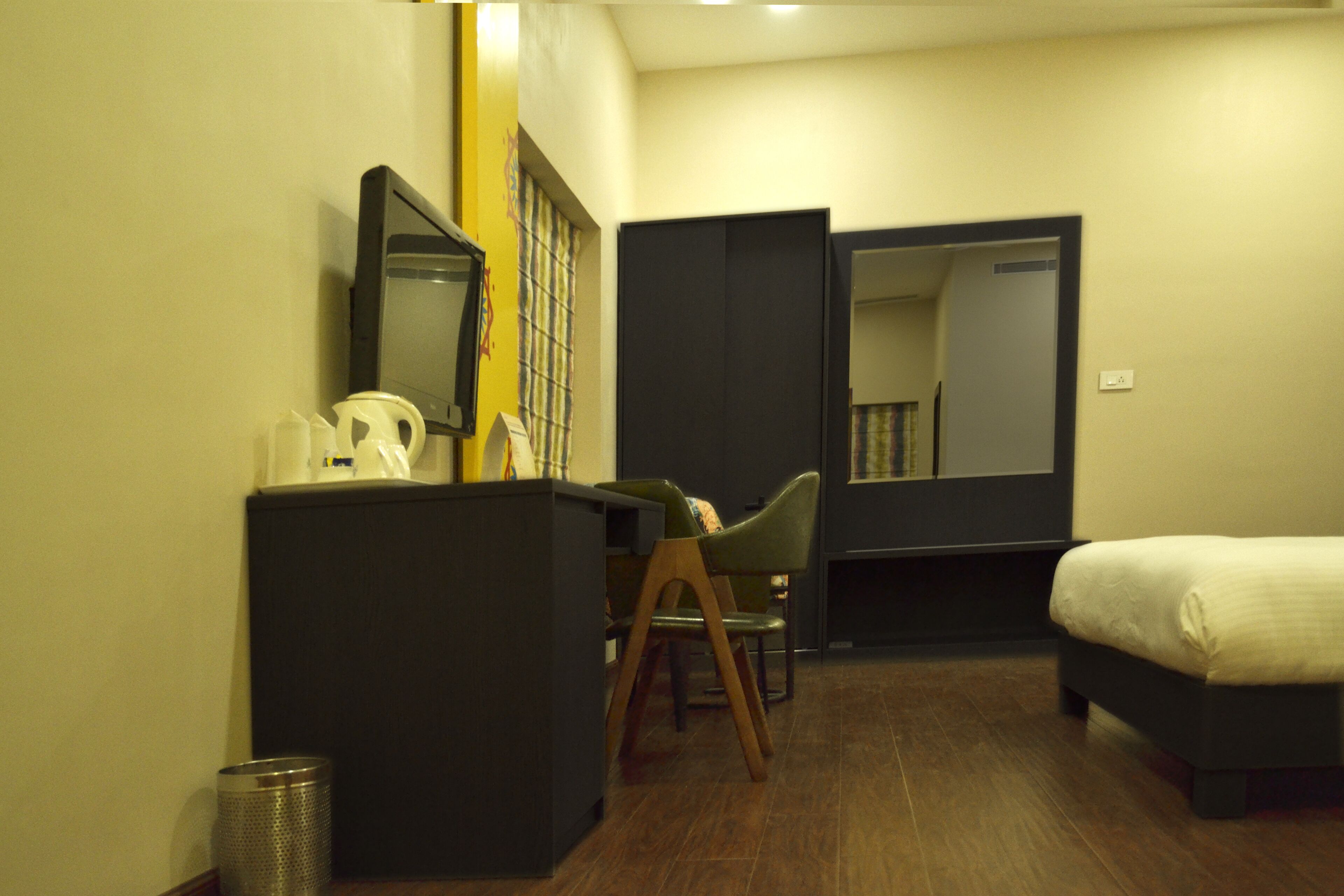 A hotel room with a bed, a desk with a chair, a trash bin, and a mirror on the wall.