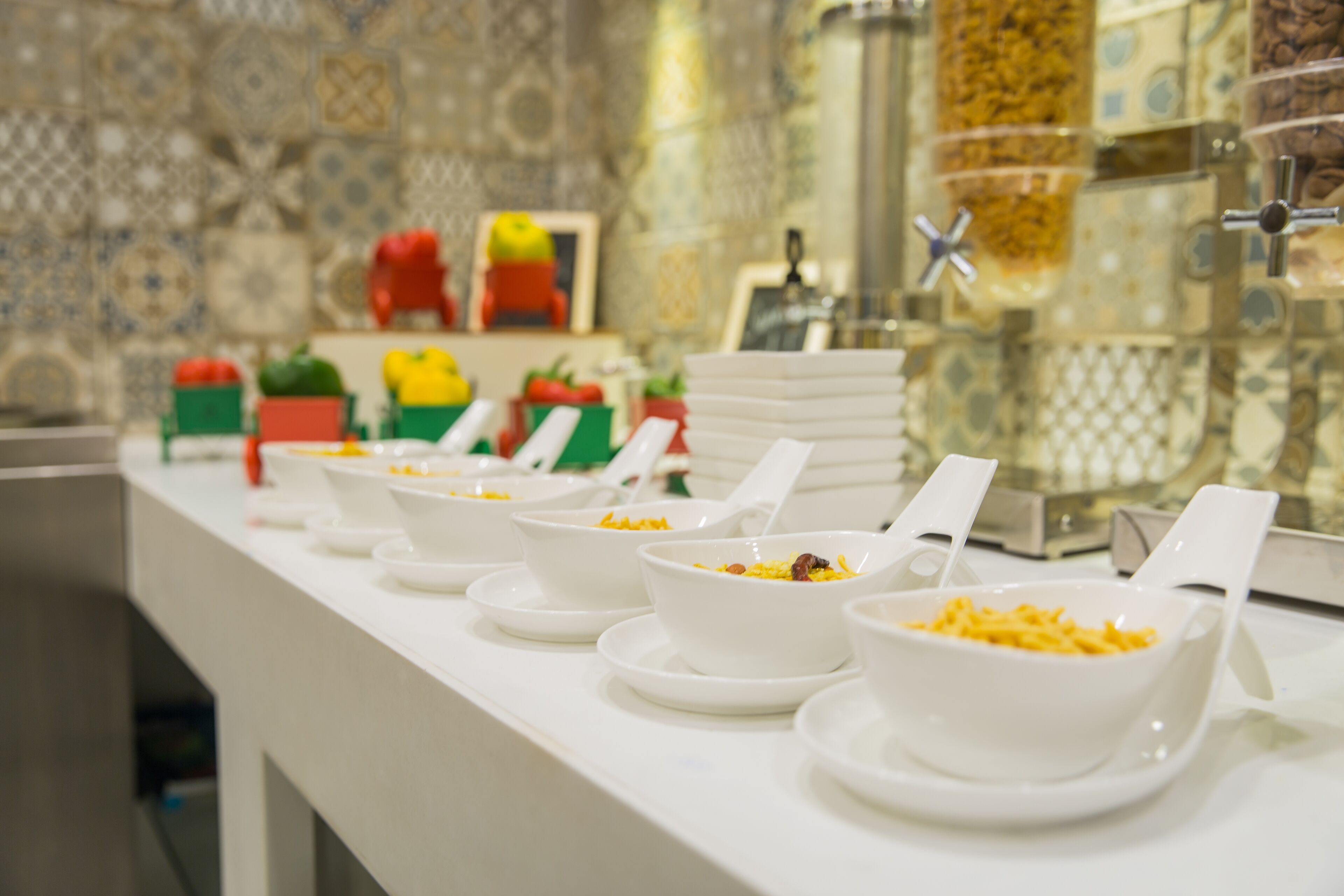 A buffet setup with multiple bowls of food on a white counter, surrounded by decorative tiles and a patterned wall.