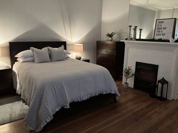A bedroom with a large bed, a nightstand, a dresser, a fireplace, and a wall with a motivational quote.