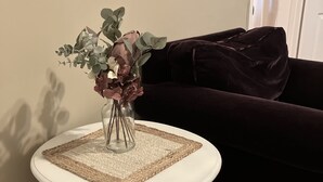 A white table with a woven placemat, a vase with flowers, and a dark-colored sofa in a room with wooden flooring and a plain wall. - Mt. Adams - Rare Gem! Minutes to Downtown (Cincinnati)