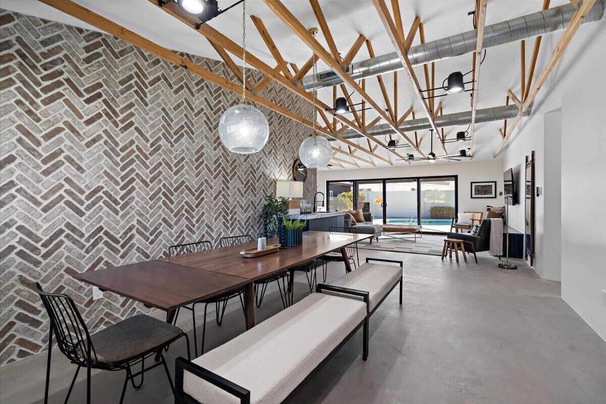 A modern dining area with a herringbone-patterned wall, a wooden ceiling with exposed beams, and pendant lighting.
