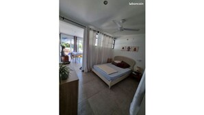 A bedroom with a bed, a ceiling fan, and a view of the outside.