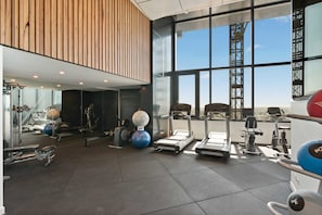 A modern gym with exercise equipment, large windows, and a high ceiling. - 60F 3BR | Stunning City & River Views (Brisbane City)