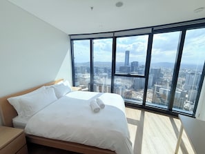A modern bedroom with a large bed, a nightstand, and a view of a cityscape through floor-to-ceiling windows. - 60F 3BR | Stunning City & River Views (Brisbane City)