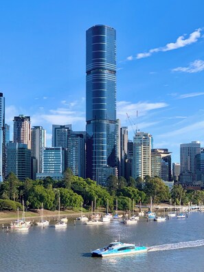 A modern skyscraper with a glass facade, surrounded by other high-rise buildings, a marina with boats, and a clear blue sky. - 60F 3BR | Stunning City & River Views (Brisbane City)
