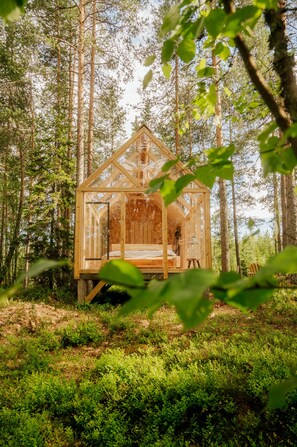A wooden cabin in a forest with a bed and a lantern. - Nordic Island Hideout Glamping Resort (Kuopio)