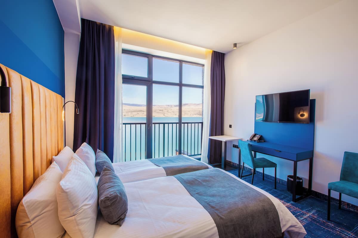 Une chambre d’hôtel avec deux lits, un bureau, une chaise, une télévision et un balcon avec vue.