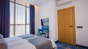 A hotel room with a bed, a desk, a chair, and a wooden door. - Gino Seaside Tbilisi, Trademark Collection by Wyndham (Tbilisi)