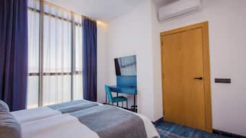 A hotel room with a bed, a desk, a chair, and a wooden door.