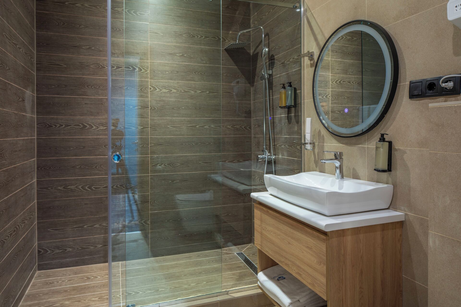 A modern bathroom with a glass-enclosed shower, a white sink, and a wooden vanity.