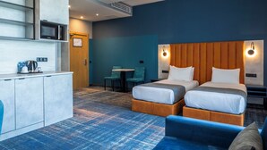 A hotel room with two beds, a kitchenette, a seating area with a table and chairs, and a blue carpeted floor.