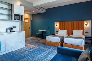 A hotel room with two beds, a kitchenette, a seating area with a table and chairs, and a blue carpeted floor.