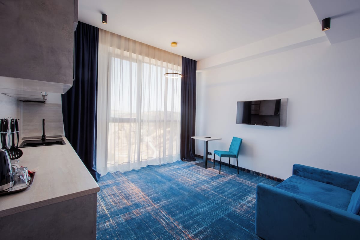 Une chambre d’hôtel moderne équipée d’une kitchenette, d’un canapé bleu, d’une petite table et d’un téléviseur fixé au mur.
