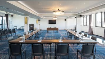 A conference room with a long table, chairs, a podium, and a large screen.
