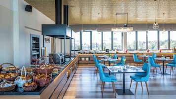 A modern dining area with a long counter, blue chairs, and a view of the city through large windows.