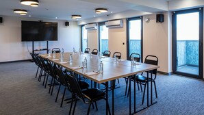 A conference room with a long table, chairs, a flat-screen TV, and large windows.