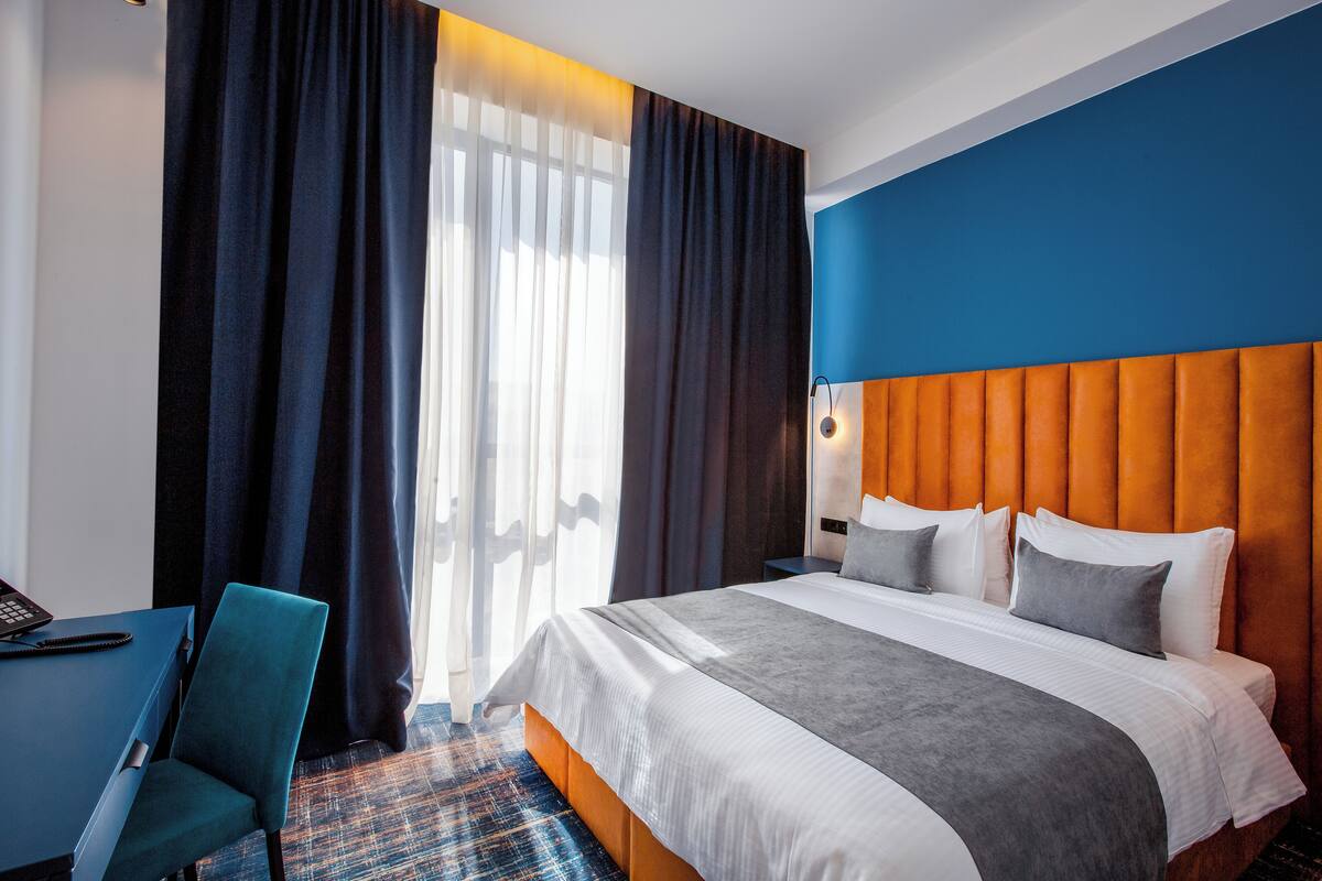 Une chambre d’hôtel avec un grand lit, un bureau avec une chaise et une vue sur l’extérieur.