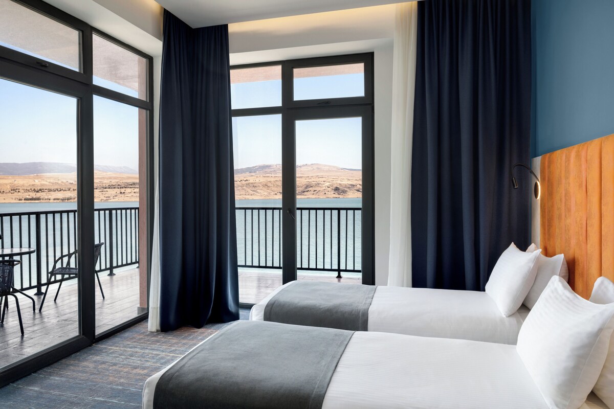 A hotel room with two beds, a balcony, and a view of a desert landscape.
