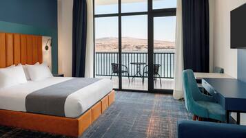 Habitación de hotel con una cama grande, un escritorio, una silla y un balcón con vistas al desierto.