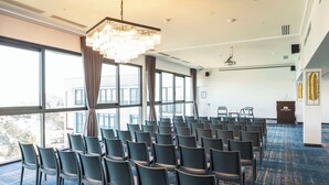 A conference room with rows of chairs, a large chandelier, and a view through large windows.