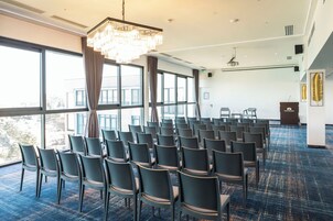 Un salón de conferencias con filas de sillas, una lámpara de araña grande y vistas amplias a través de ventanas grandes.