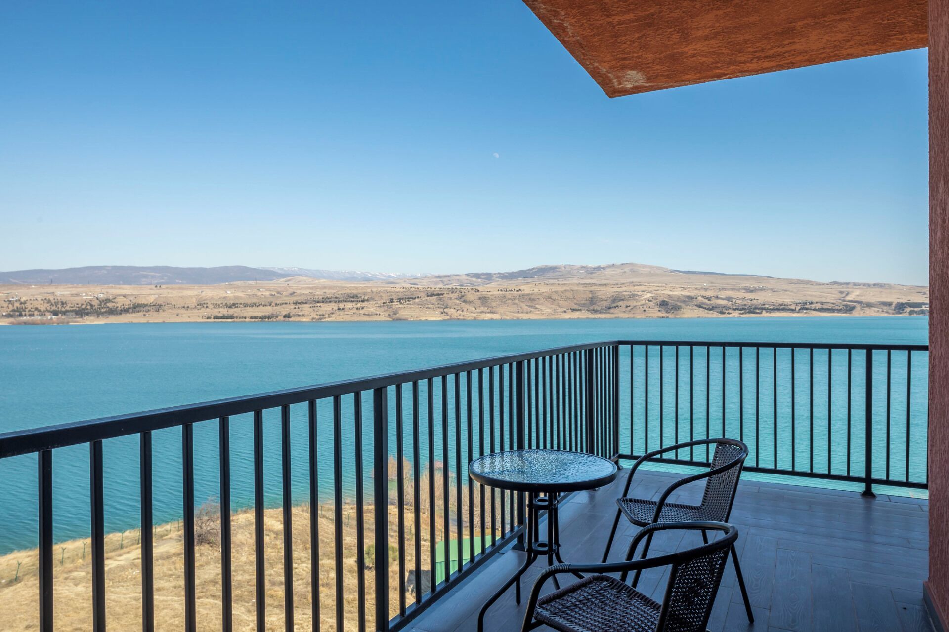 Balcón con mesa y sillas con vista a un cuerpo de agua y colinas lejanas.