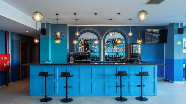 A bar area with a blue counter, four stools, and a variety of bottles and glasses.