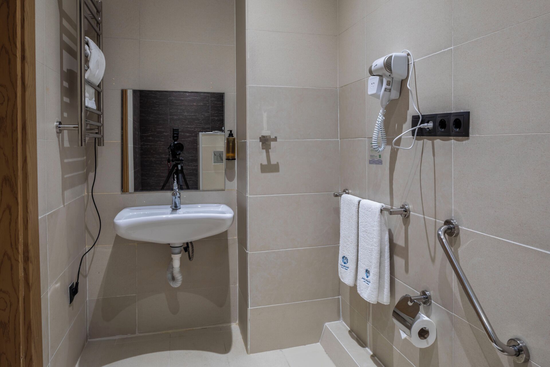 Un baño con lavamanos, espejo, toallero, secador de pelo y dispensador de papel higiénico.