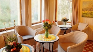 A cozy room with wicker furniture, a tiled floor, and large windows with curtains.