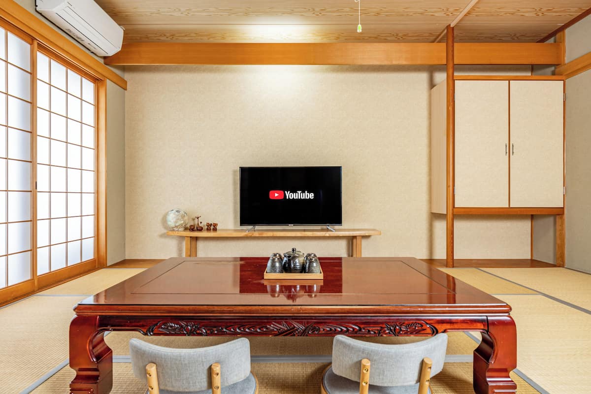 A traditional Japanese room with tatami flooring, a wooden table with chairs, a television on a stand, and a wardrobe.