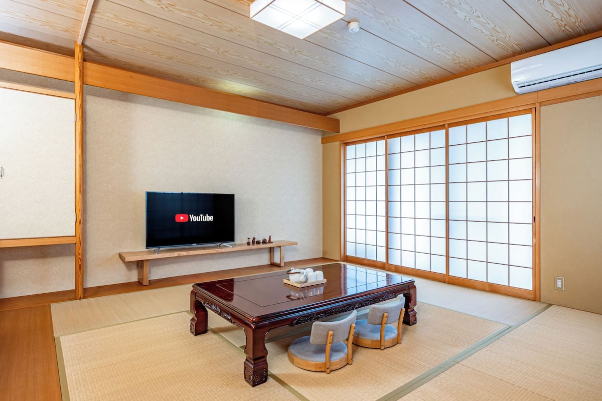 A traditional Japanese room with tatami flooring, a low wooden table, a television, and a sliding door with a grid pattern.