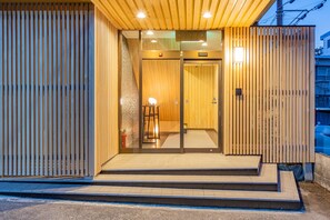 A modern building entrance with a wooden facade, glass doors, and a small outdoor seating area. - Azami Ann (Shirahama)