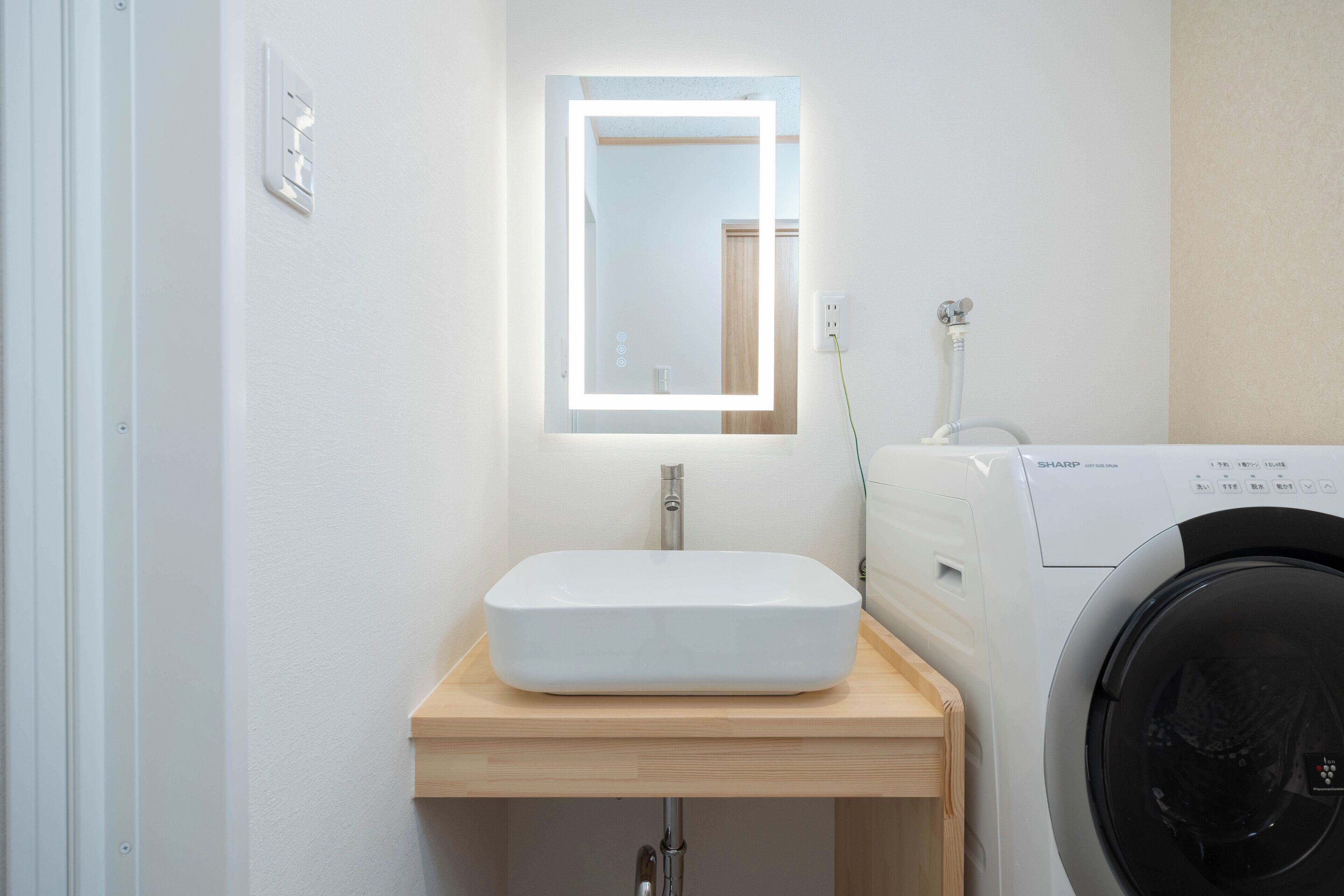 A bathroom with a white sink, a mirror with a light, and a washing machine.