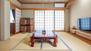 Ein traditioneller japanischer Raum mit Tatami-Bodenbelag, einem niedrigen Holztisch und einem Fernseher auf einem hölzernen Standfuß.