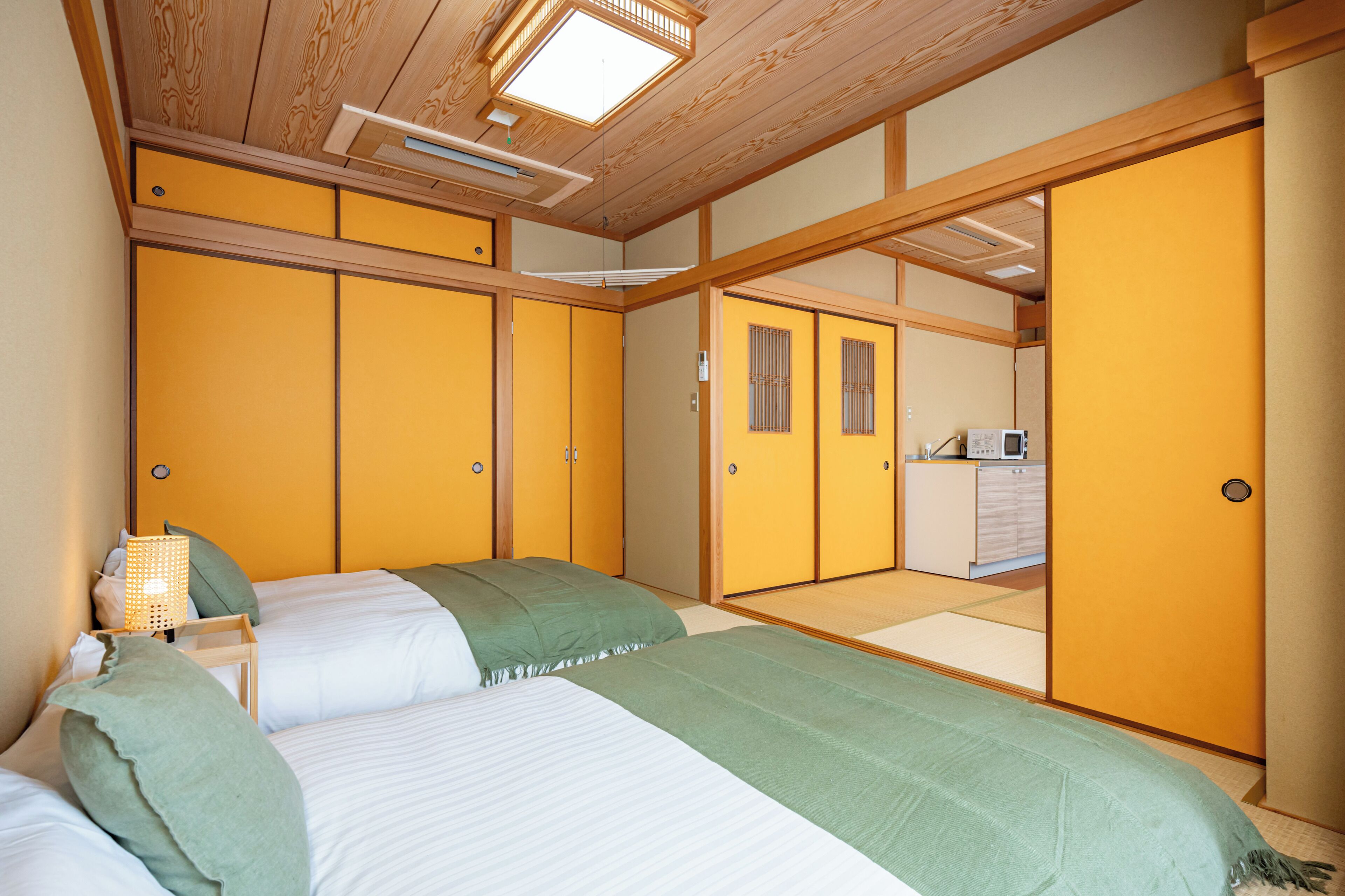 Ett traditionellt japanskt sovrum med tatamimattor på golvet, en futonmadrass och skjutdörrar som leder in till ett köksområde.