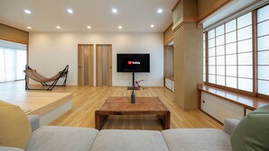 Ein modernes Wohnzimmer mit Holzboden, einem an der Wand befestigten Flachbildfernseher, einer Hängematte und einem großen Fenster.