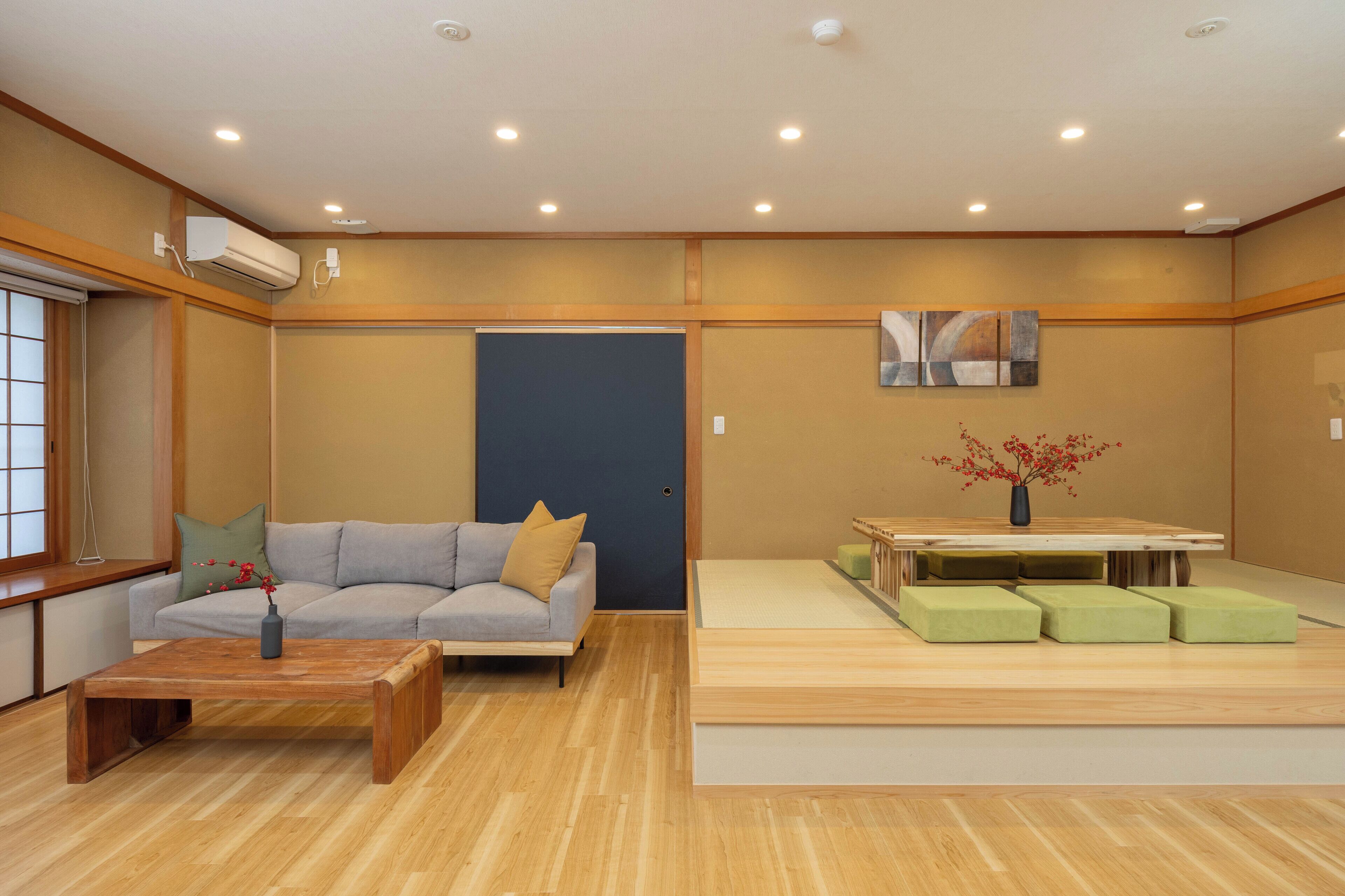 A modern living room with a sofa, coffee table, and a dining area with a table and green ottomans.