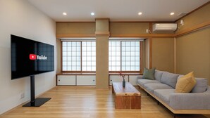 Ein modernes Wohnzimmer mit Flachbildfernseher, einer Couch, einem Couchtisch und großen Fenstern.