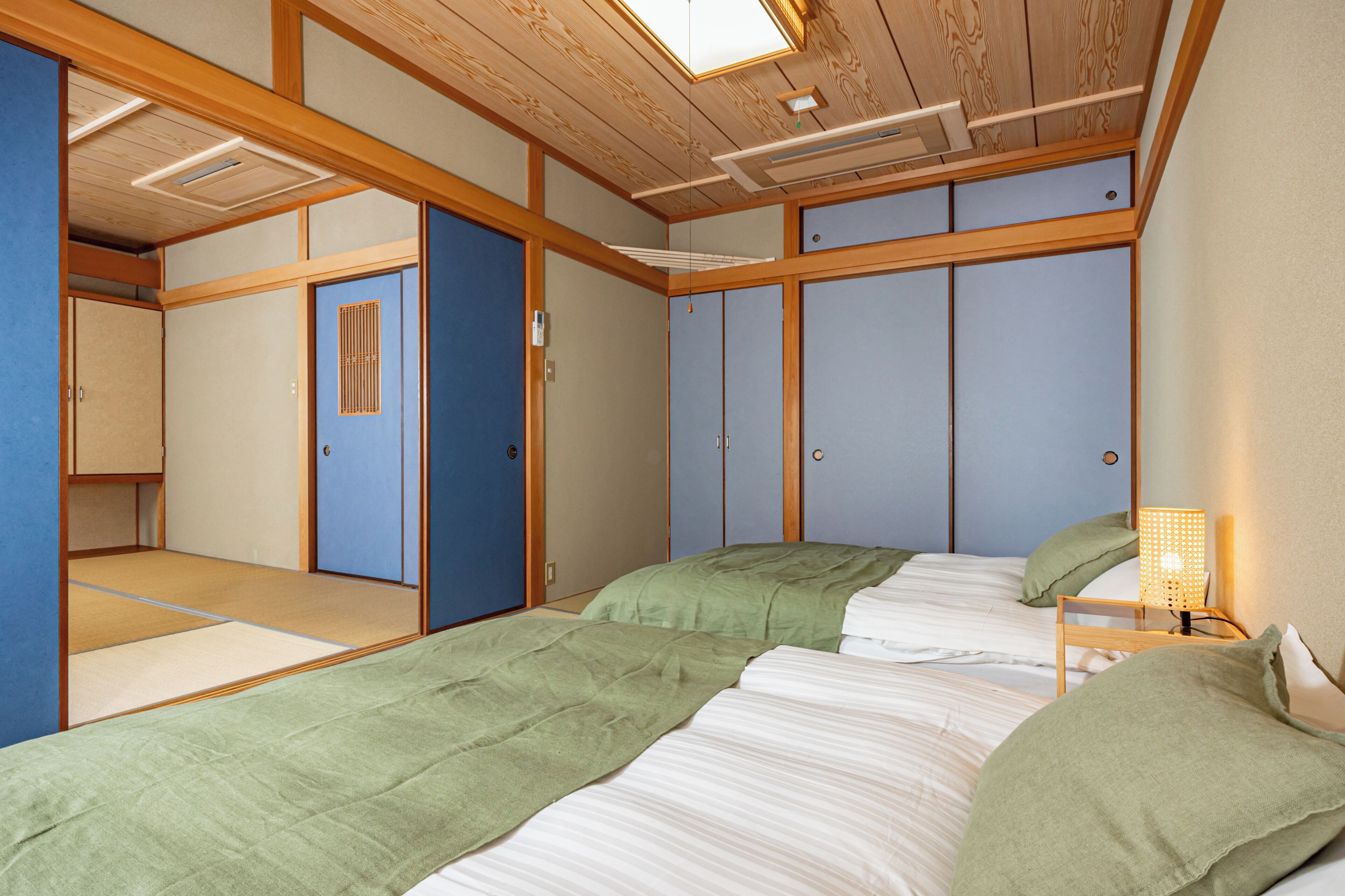 A traditional Japanese-style room with tatami flooring, a sliding door, and a bed with green bedding.