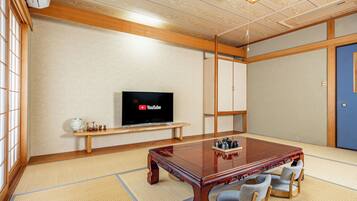 Perinteinen japanilaistyylinen huone, jossa on tatamimatto, puinen pöytä ja tuolit, televisio ja kaappi.