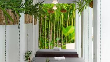 A series of massage tables arranged in a row under a wooden ceiling with hanging plants and a hanging light fixture.
