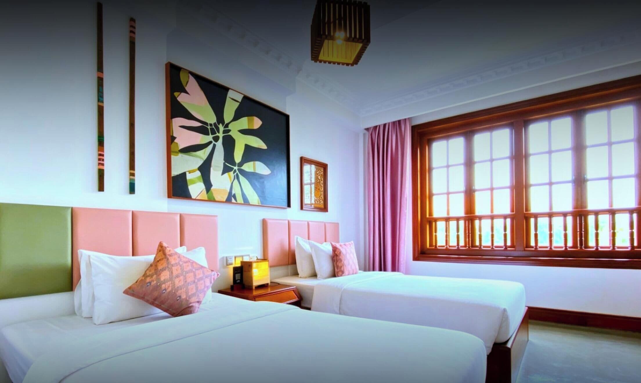 Une chambre d’hôtel avec deux lits, une grande fenêtre et un tableau au mur.