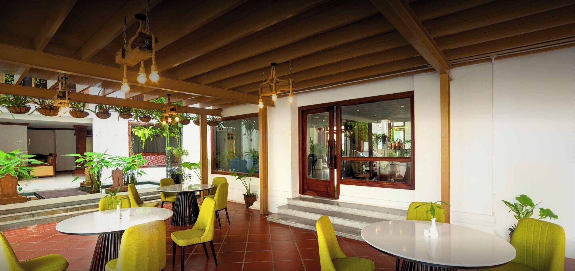 A covered outdoor seating area with tables and chairs, potted plants, and a view of the interior through a glass door.