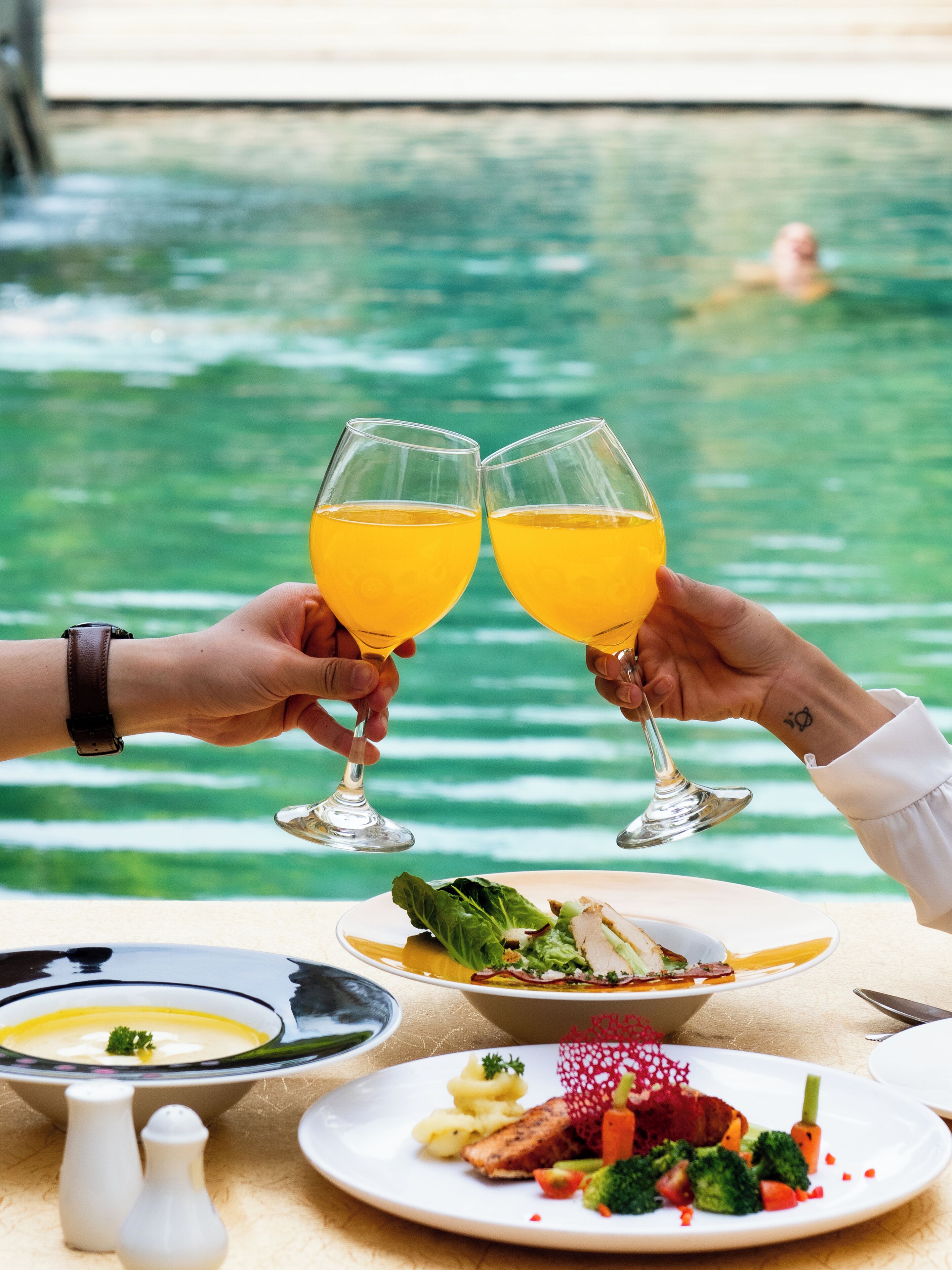 A dining table with a meal and two glasses of orange juice, overlooking a pool.