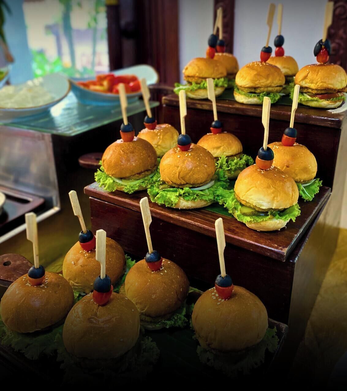 Une présentation de mini-burgers et de tranches de pommes, maintenues ensemble par des cure-dents, disposées sur une planche en bois.