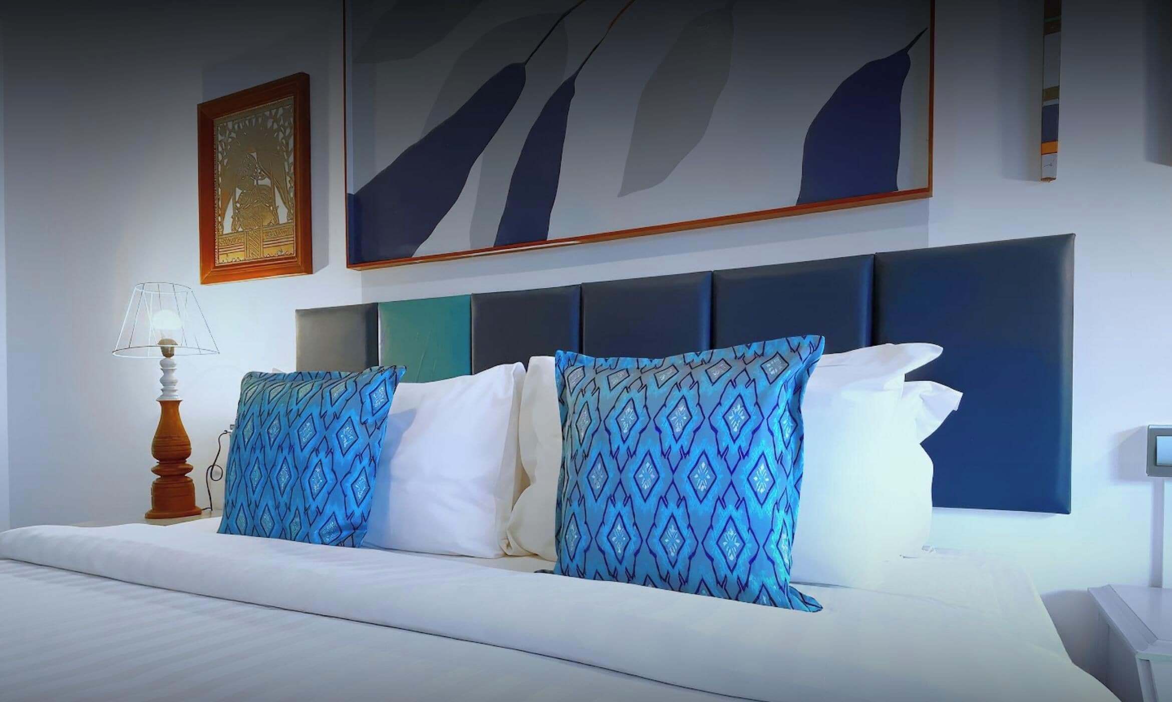 Habitación de hotel con cama, mesita de noche, lámpara y una obra de arte en la pared.