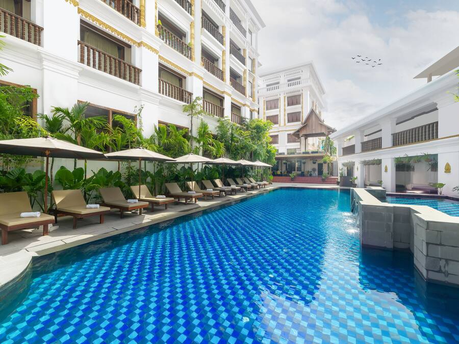 A swimming pool with lounge chairs and umbrellas, surrounded by white buildings with balconies.