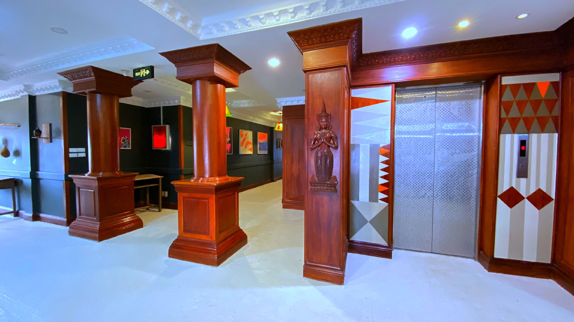 A lobby with wooden columns, a statue, and an elevator with geometric patterns.