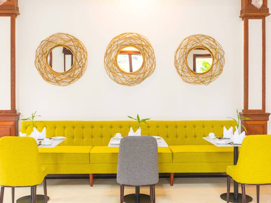 A dining area with a yellow sofa, two yellow chairs, a gray chair, and three woven mirror decorations on the wall.